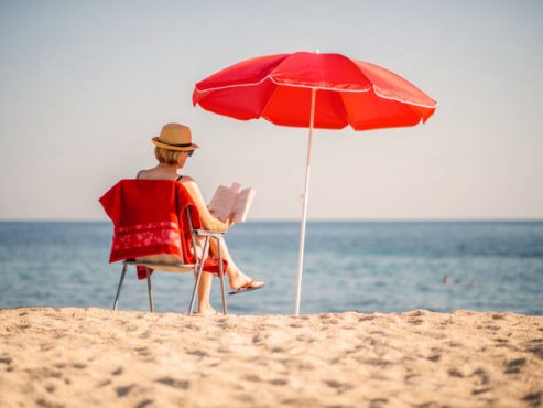 Woman reading book in deck chair under sun umbrella near sea